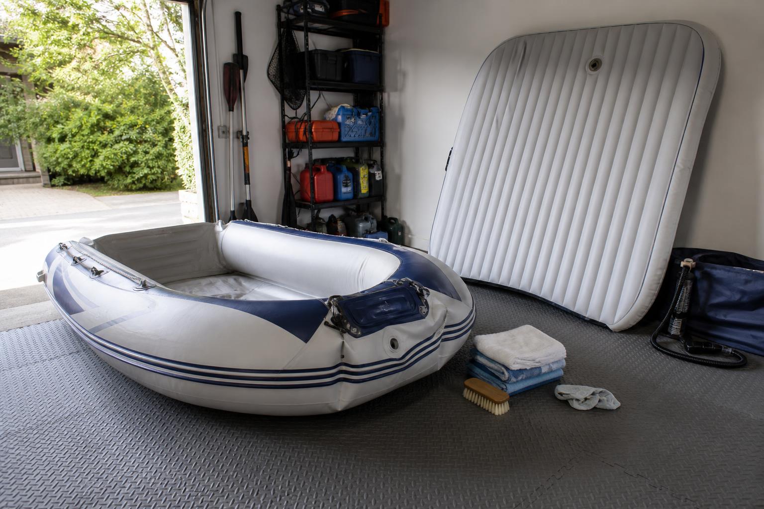A practical garage storage scene showing a clean inflatable boat partially inflated on a padded floor, with its air floo