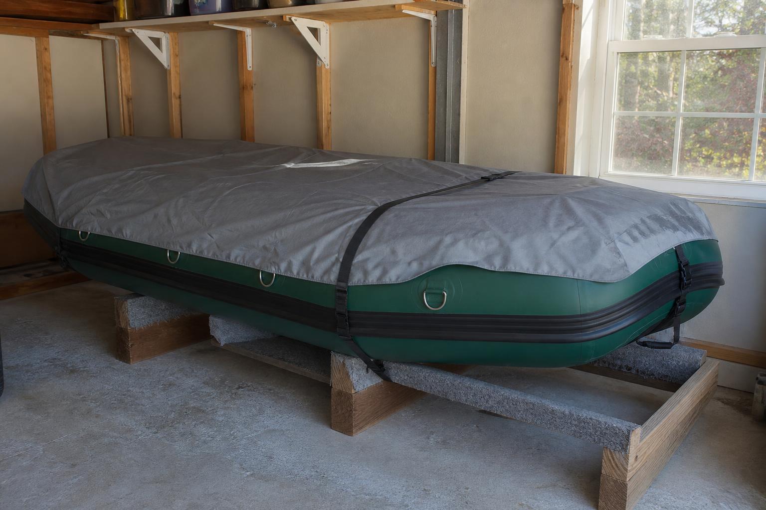 A tidy garage or carport scene with a covered inflatable raft resting on a rack, slight incline visible for drainage, so