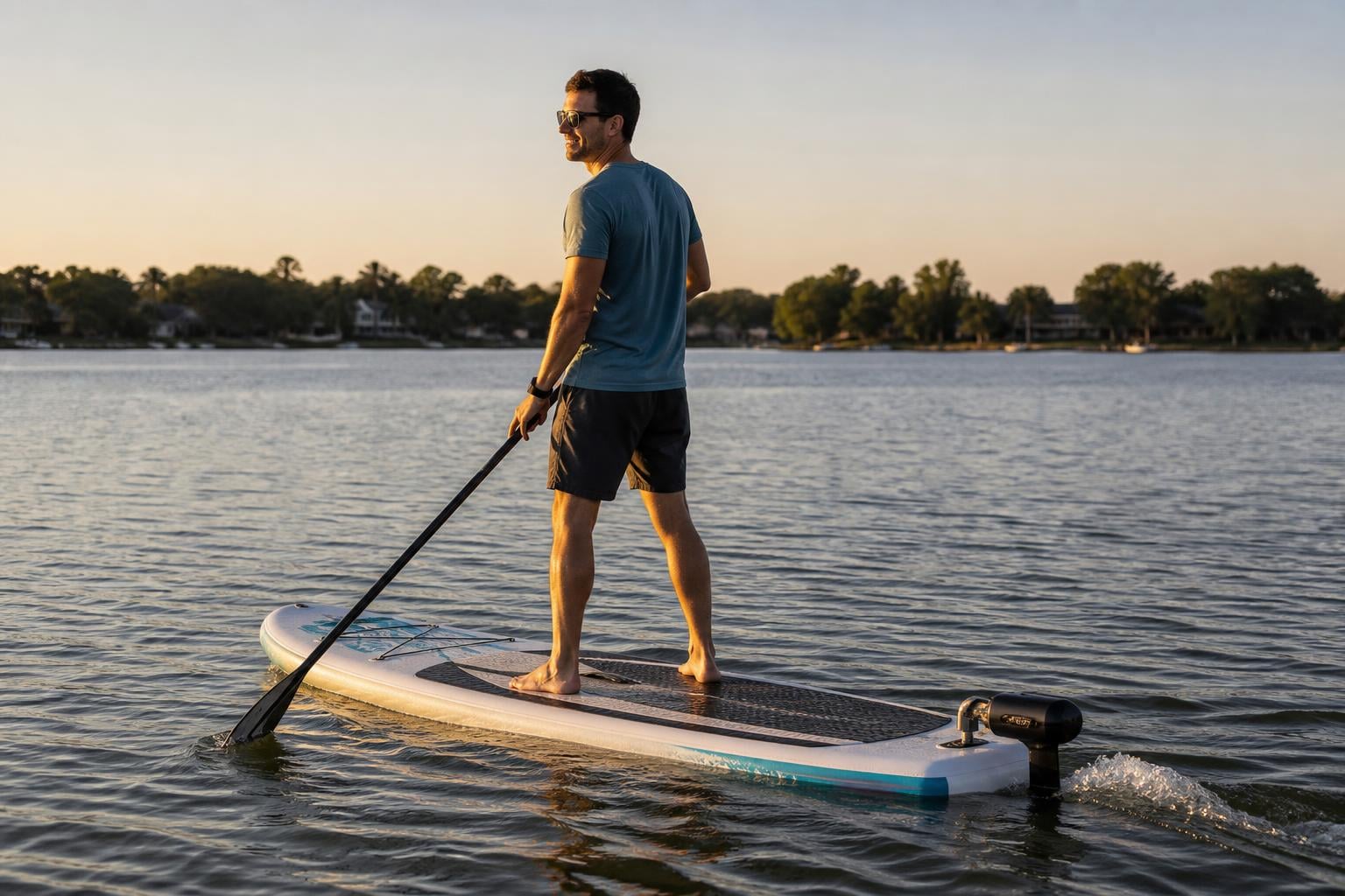 Person on an inflatable stand-up paddle board on a calm lake at golden hour, wearing a wrist remote control, with a smal